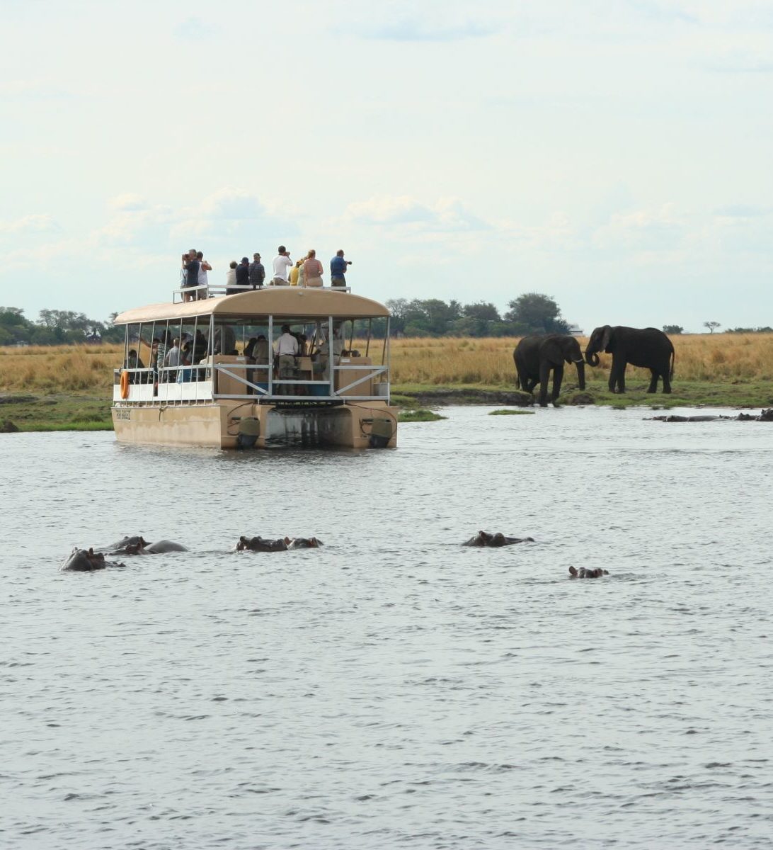 Rondreis Botswana, Chobe National Park, waterplaats met nijlpaarden en olifanten en boot op het water